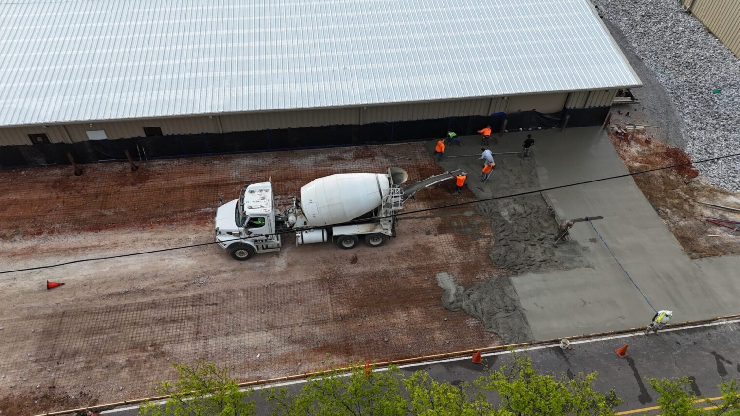 Concrete truck pouring slab while workers finish
